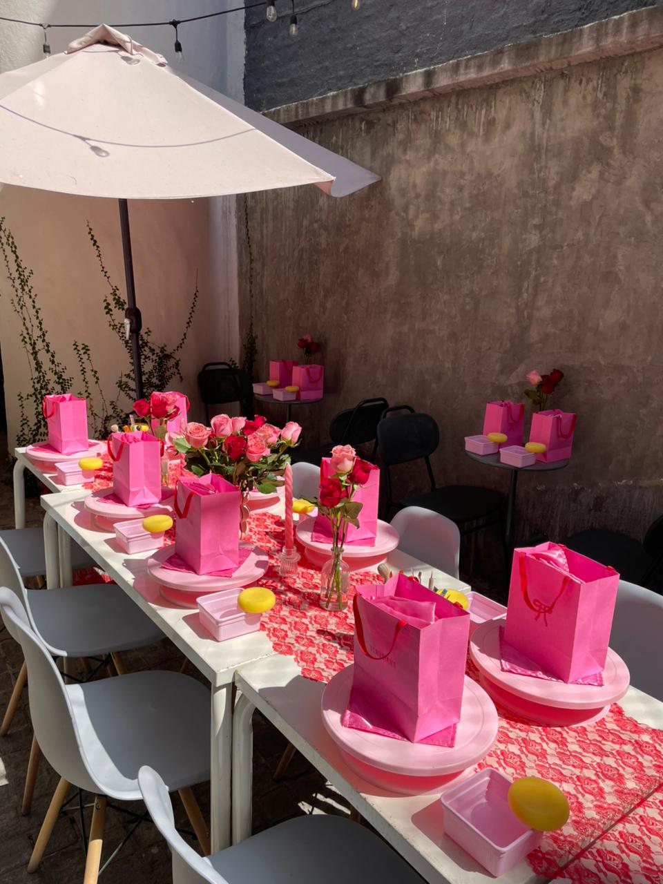 Mesa del taller decorada con flores, manteles rosas y bolsas de regalo